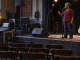A vocalist listens and gestures to a sound engineer during a microphone check in an empty small venue.