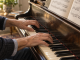 A pianist practices a short marked passage with both hands on an acoustic piano in daylight.
