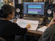 An artist points to one marked section of a song map while reviewing a mix with an engineer in a project studio.