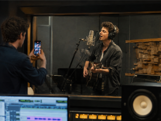 Singer recording while a collaborator documents the studio session