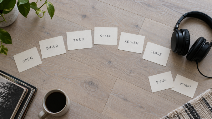 Handwritten song-role cards form a curved running order beside headphones on a pale wood surface.