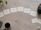 Handwritten song-role cards form a curved running order beside headphones on a pale wood surface.