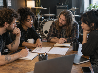 Four band members sit around a rehearsal-room table reviewing a concise decision list and shared calendar.