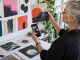 An older songwriter compares an abstract square cover print with several tiny cover thumbnails on a phone.