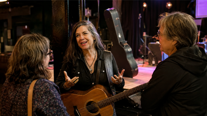 Guitarist speaking naturally with listeners beside a small venue stage