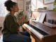 A pianist pauses to recall a melodic phrase before testing notes at an upright piano.